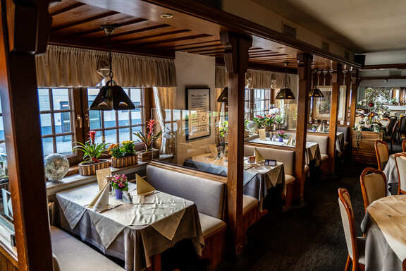 Cosy rustic restaurant interior with wooden beams, carefully set tables, bench seating and flowers by the window.